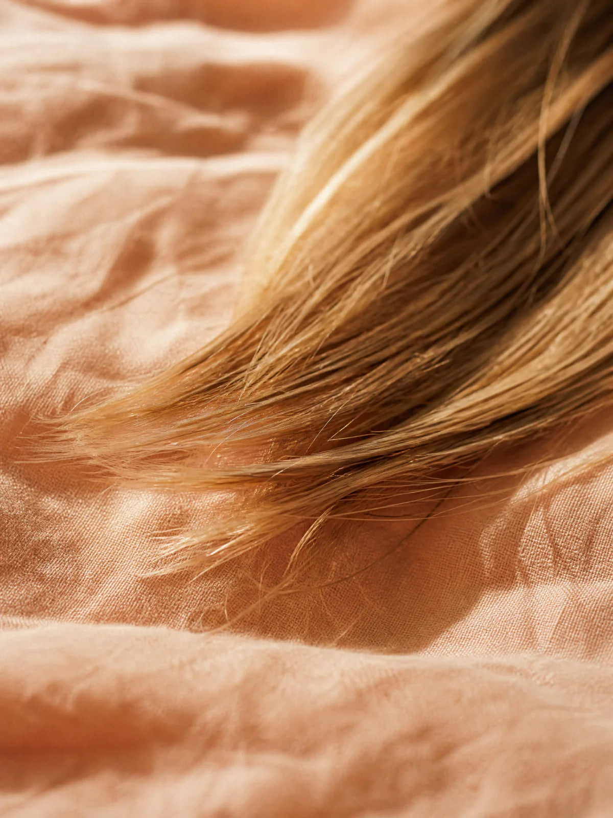Cheveux abîmés réparés - pointes caramel blondes saines sur linge pêche